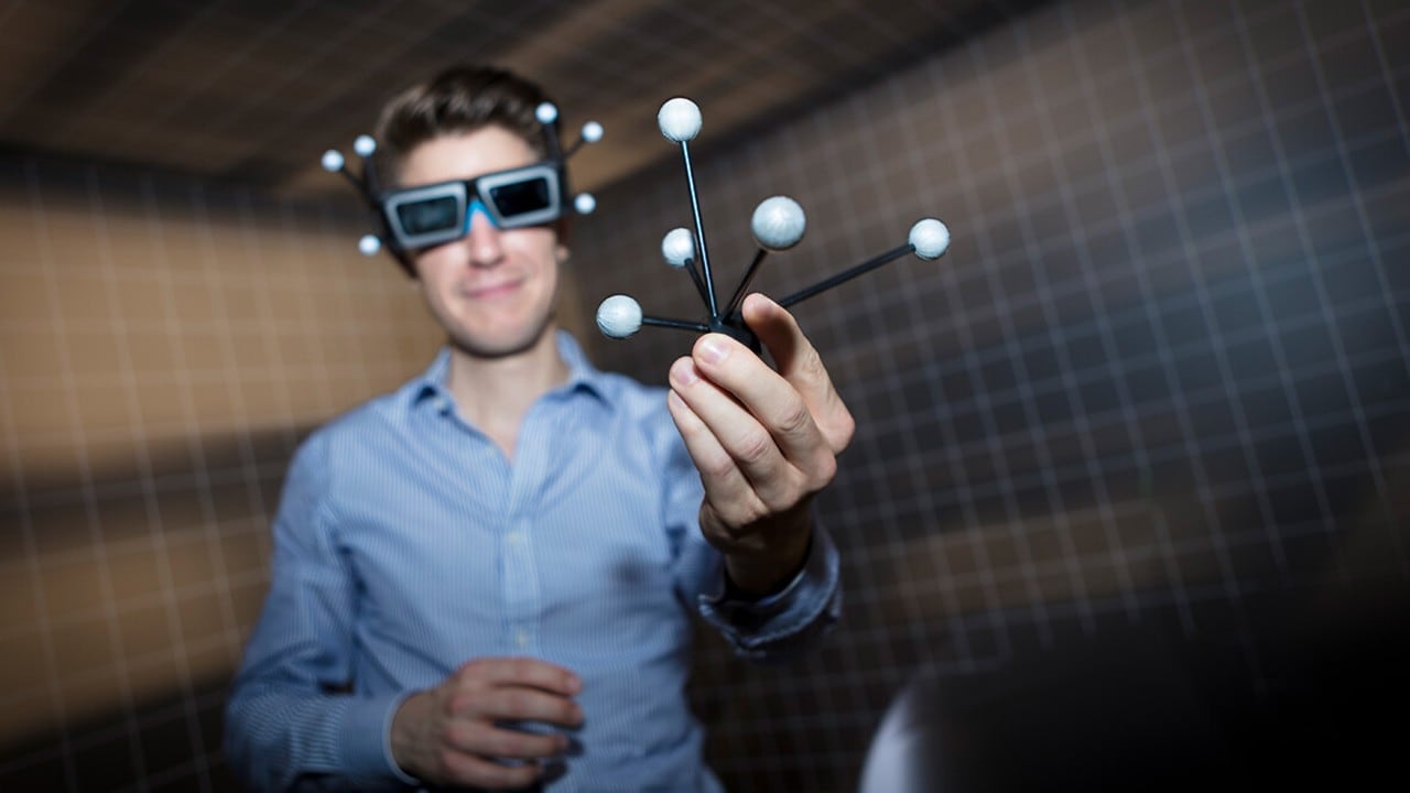 Ein junger Mann mit Datenbrille hält Atom-Bausteine vor sich